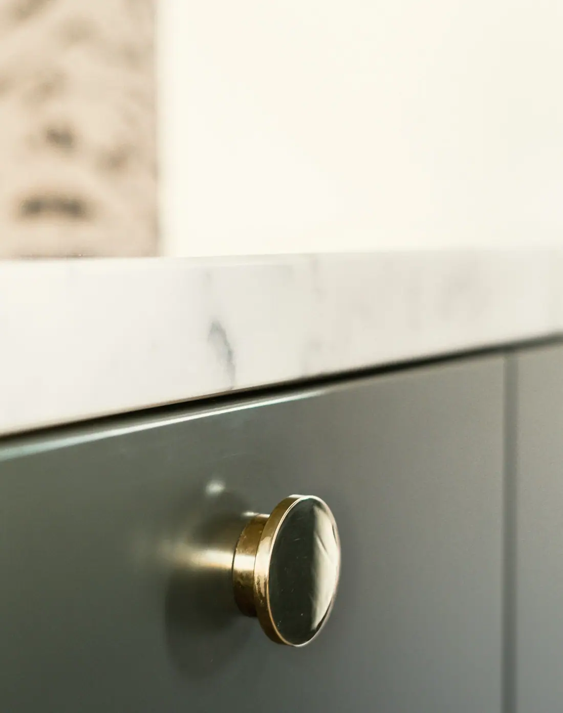 Brass knob on a sage green cabinet under a marble worktop