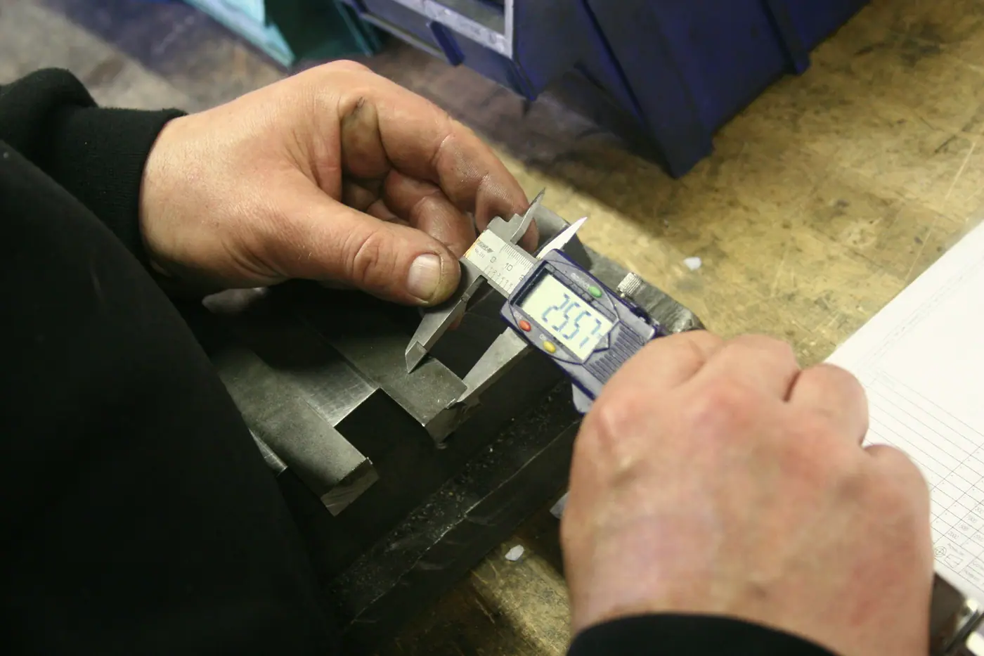 Hands measuring a brass part with a digital caliper