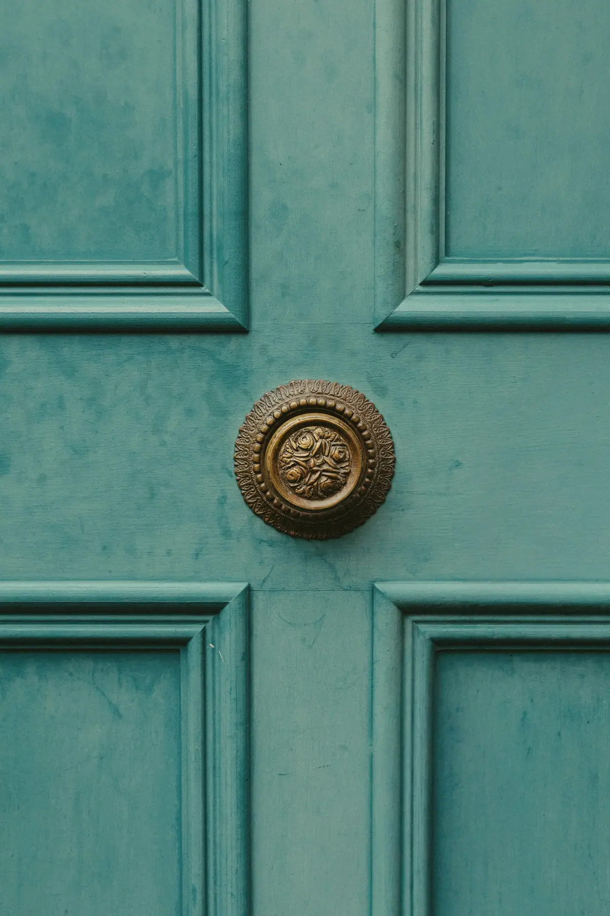 Ornate brass knob on a teal panelled front door